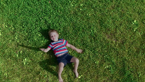 The cheerful boy lies on the grass. 