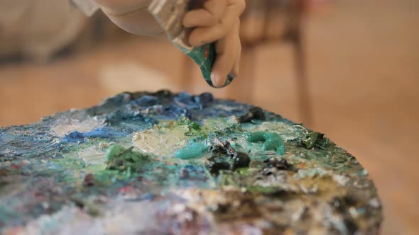 Artist Puts Green Paint on Palette From Tube in Studio alt