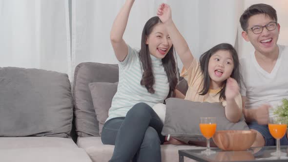 Asian family watching TV and hand raised for cheer on sofa in living room