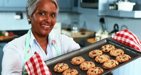 Senior woman holding a tray with homemade cookies in kitchen alt