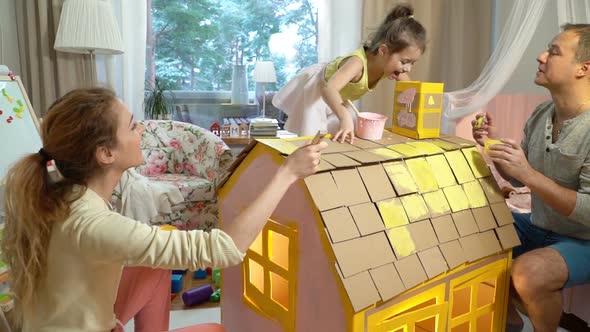 Young Family with Child Building and Painting Toy Cardboard House Together. alt