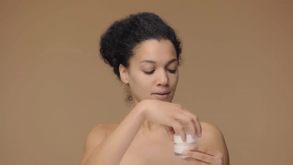 Beauty Portrait of Young African American Woman Twisting Off Jar of Cream and Dissatisfied with Its alt