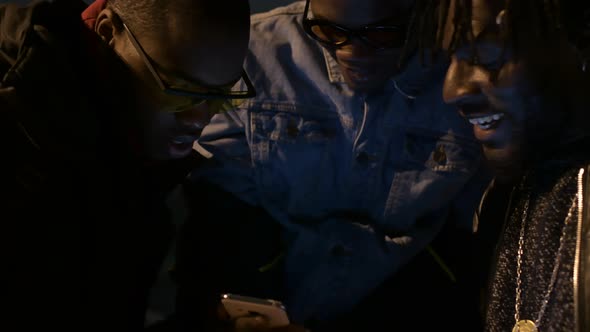 three african friends sitting outdoor and looking the smartphone alt