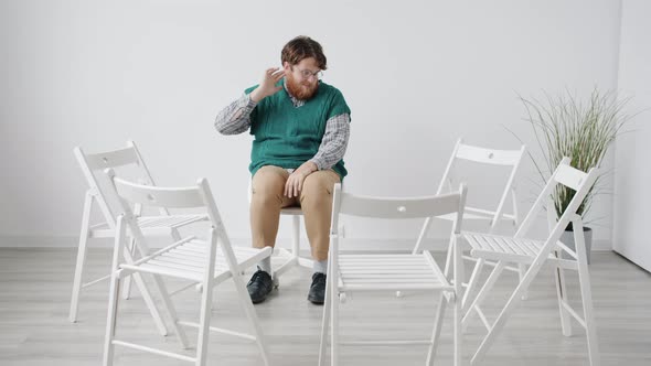 Insecure Guy Sitting in White Room Alone Waiting for Group Therapy Feeling Nervous alt