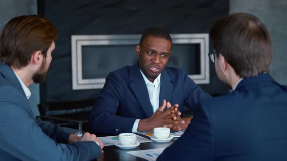 Smiling african american man in suit with colleagues at the table at meeting alt