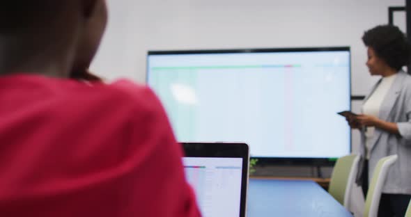 African american businesswoman using tablet presenting at screen to female colleague at meeting alt