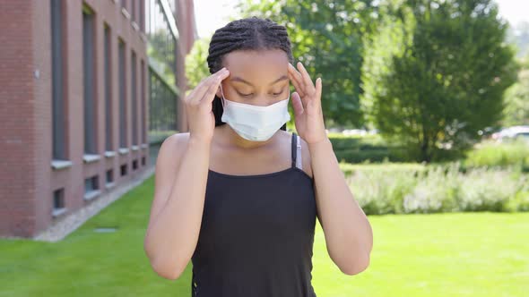 A Young Black Woman in a Face Mask Is Sick, Coughs and Has a Headache - an Office Building alt