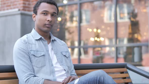 Young African Man Smiling While Sitting on Bench alt