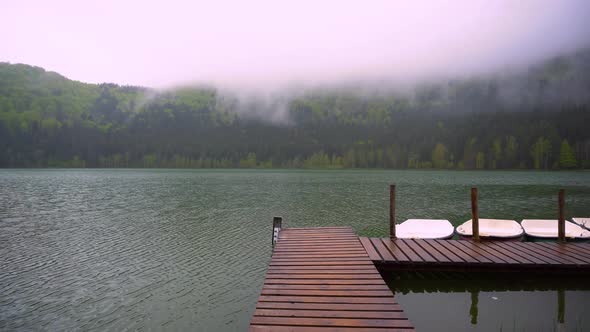 Boats floating on the lake close to the wooden pier. Smooth calm surface of mountain lake alt