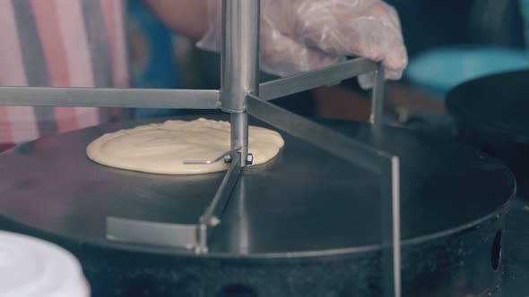 Cooker Puts Dough on Hot Stove and Spreads with Turning Tool alt
