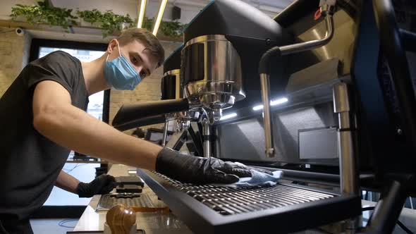 Concentrated Male Barista in Coronavirus Face Mask Cleaning Coffee Machine in Cafe alt