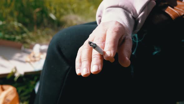 Woman Holding a Cigarette in Hands Sitting in Nature on Sun on Sunset alt