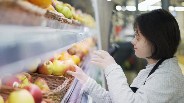 Woman with Down Syndrome Restocking Fresh Fruits in a Grocery Store Side View alt