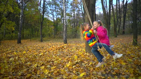 Two girls riding on a swing in the fall in nature in the Park