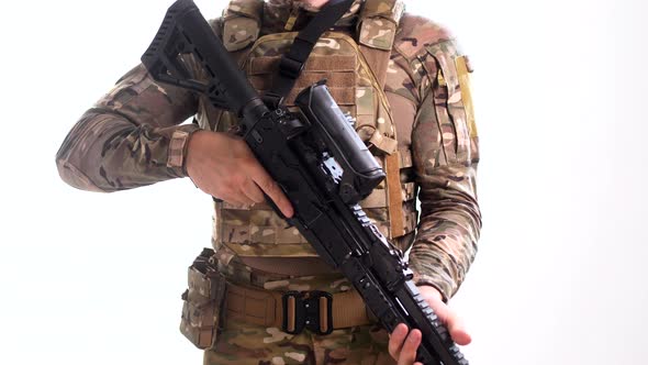 Man in combat camouflage and body armor picks up an assault rifle and hangs it on his belt