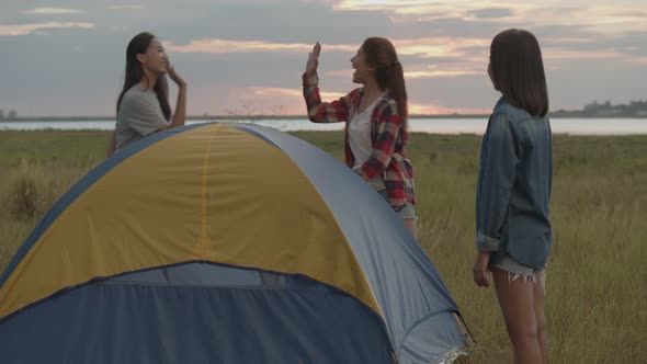 Asian women camping pitch a tent while sunset enjoying having fun together a summer traveling.