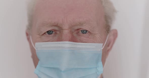 Portrait of Senior Man with Medical Mask on Face Looks Up Sadly Into Camera alt