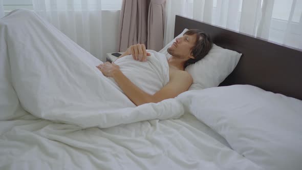 A Young Man in a Bed Puts on a Teeth Guard Before Going To Sleep. Anti Grinding Teeth Protector alt