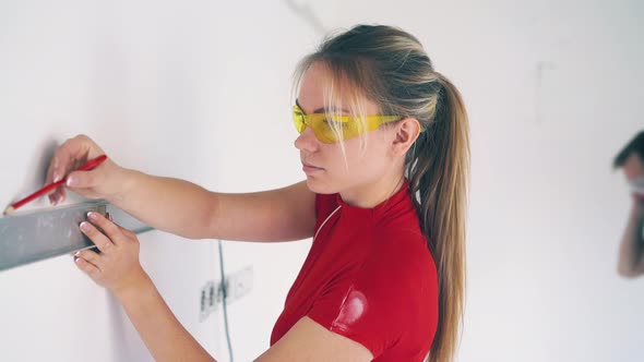 Girl Draws Line on Wall with Level Against Man in Light Room alt