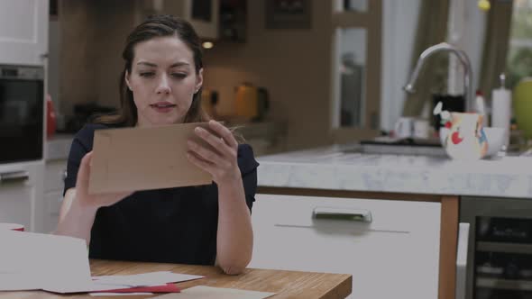 Young adult woman opening bills at home on kitchen table