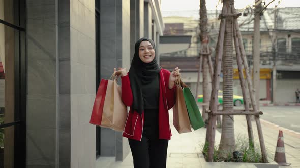 young Muslim woman happily carries a shopping bag on the street after returning from shopping