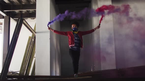 Mixed race man holding blue and purple flares walking through an empty building alt