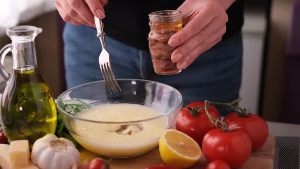 Making Caesar Salad Sauce  Woman Adding Anchovies Into Glass Bowl alt