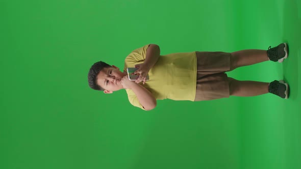 Full Body Of Asian Little Boy Use Mobile Phone And Thinking On Green Screen In The Studio alt
