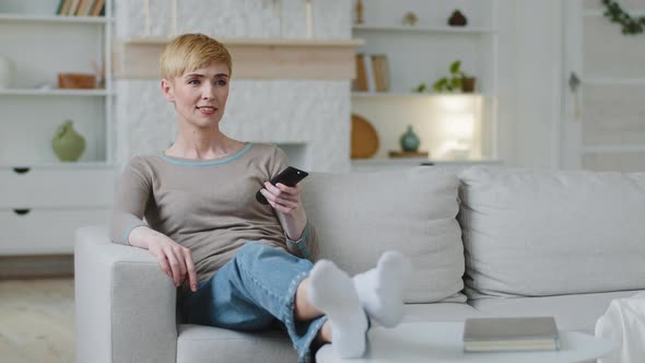 Single Woman Resting Lean on Comfortable Cozy Couch Cushions Hold TV Remote Control Switch Digital alt