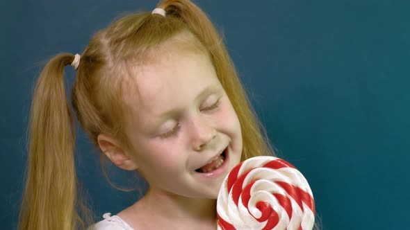 Little Girl with a Lollipop on a Blue Background. Close Up Portrait
