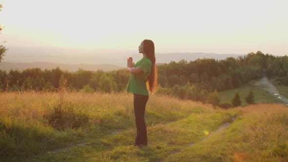 Serene Lovely Asian Female with Eyes Closed Meditating in Prayer Yoga Pose on Mountain Top at Dawn alt
