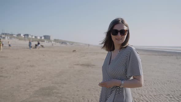 A Woman in a Dress Walks on an Ocean Beach on a Windy Sunny Day