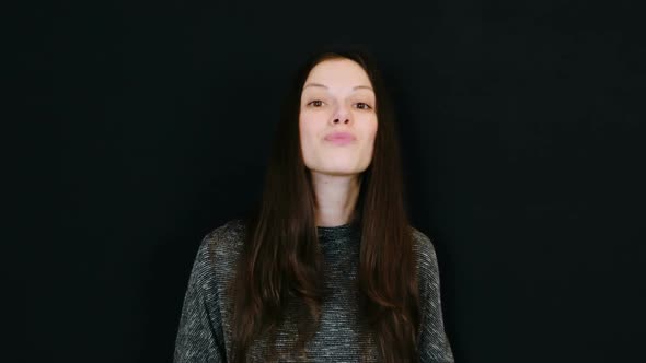 Young Brunette Woman Sends a Lot of Kisses Looking at the Camera in Black Background