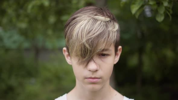 Portrait of a Boy with a Stylish Hairstyle Looking at the Camera and Smiling Outdoors Looks Up alt