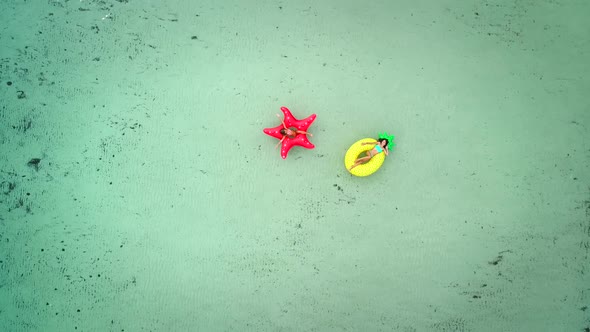 Aerial view of two girls floating on inflatable mattress in transparent sea. alt