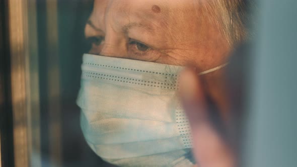 Elderly Woman at Window in Protecting Medical Mask on Selfisolation alt