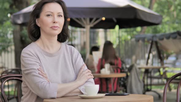 Serious Old Woman Looking in Camera while Sitting in Outdoor Café alt