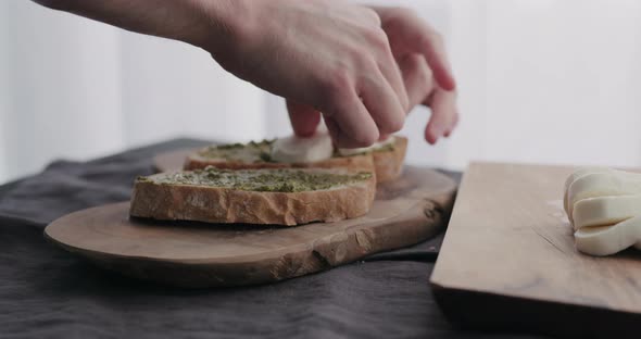 Slow Motion Man Making Ciabatta Bruschettas with Mozzarella and Pesto on Olive Board with Window on alt
