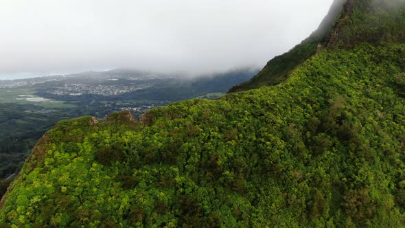 Drone flying over hawaiian mountain overlooking east oahu town on a rainy day alt
