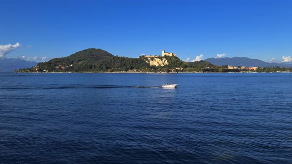 Small motorboat navigating in calm lake waters of Maggiore lake in Italy with Angera castle in backg alt