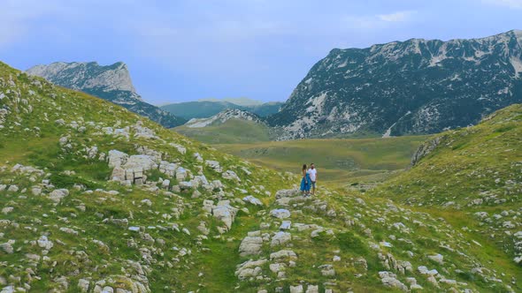 Couple Travelers Man and Woman Staing on Cliff Relaxing Mountains and Clouds Aerial View in Durmitor alt