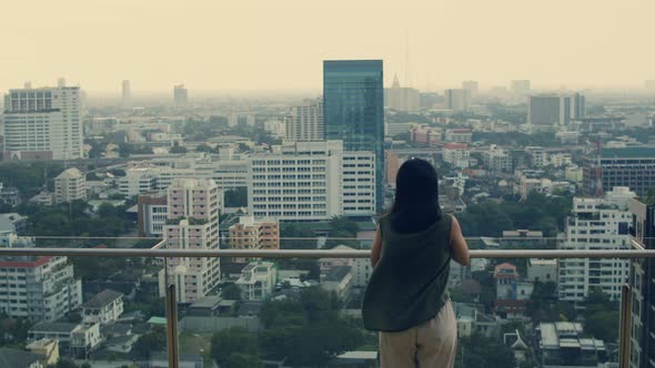 Asian woman using smartphone while standing on the rooftop building.