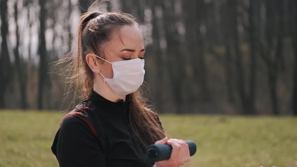 Athletic Woman in a Protective Mask Is Doing Exercise with Dumbbells alt