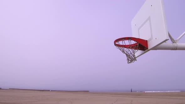 A man does a slam dunk while playing one-on-one basketball hoops on a beach court alt