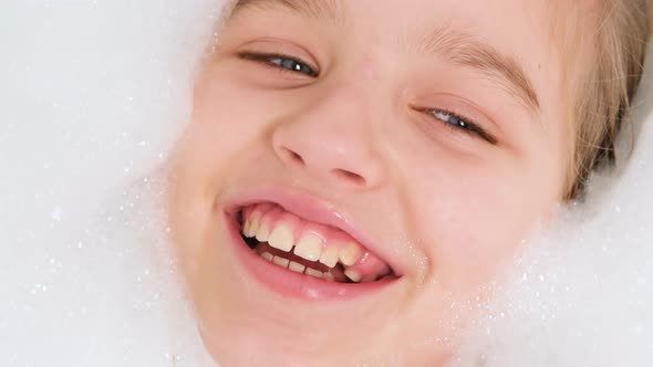 Portrait of Cheerful Teen Girl Lying in Bath with Thick Soap Foam and Looking in Camera