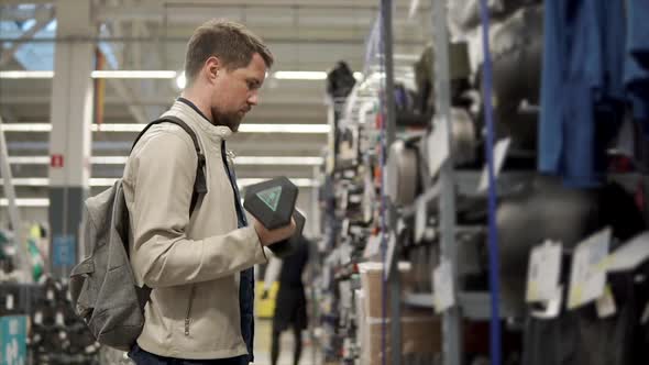Sportsman is Selecting a Dumbbell for Him in a Shop Trying Weight alt