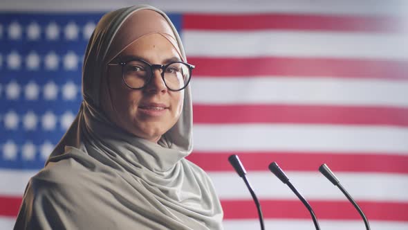 Portrait of Positive Female Politician in Hijab against U.S. Flag alt