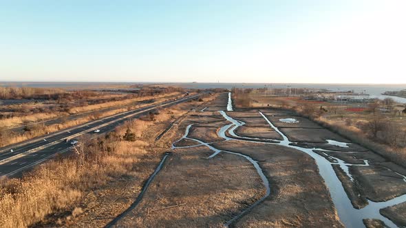 An aerial view over a marsh on Long Island, NY. A long road with a few cars run next to it, shot on alt