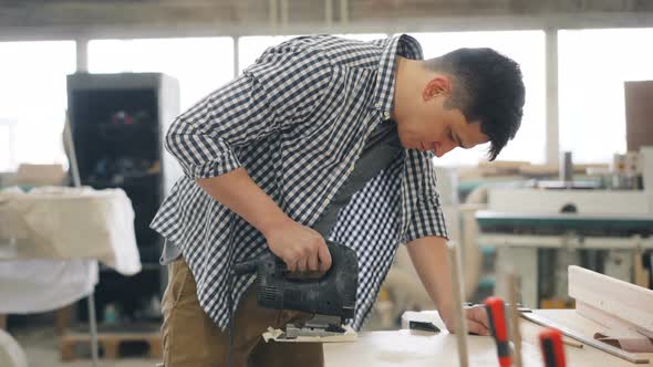 Young Carpenter Using Jigsaw Power Instrument To Saw Wood in Workshop alt