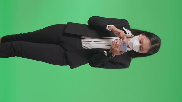 Asian Business Woman Wearing Mask Using Mobile Phone While Walking On Green Screen Studio alt